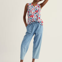 Woman wearing a floral sleeveless top and light blue pants on a white background
