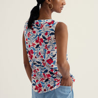 Woman wearing a sleeveless floral top and light blue pants on a plain background