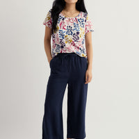 Woman wearing a colorful floral top and navy pants on a white background