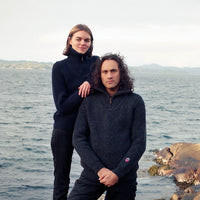Two people standing on rocks by a body of water.