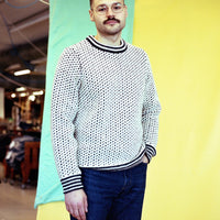 Person wearing a patterned sweater and glasses standing against a colorful background