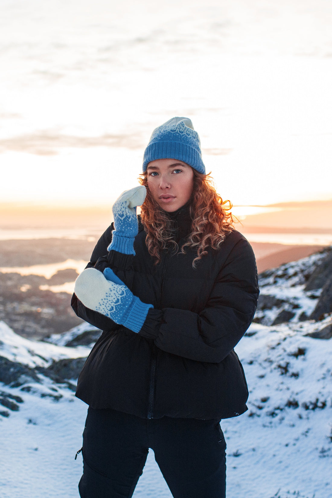 Model wears the Norlender Adult Mittens in Blue in a snowy landscape.