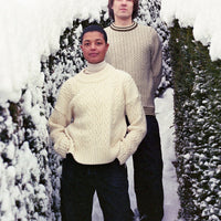 Two people standing in a snowy landscape with trees and bushes.
