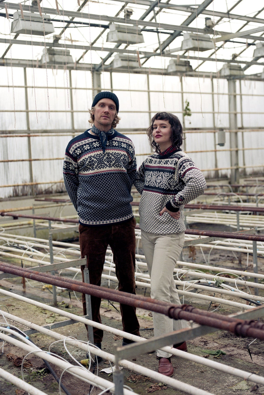 Two people wearing matching patterned sweaters in a greenhouse setting.