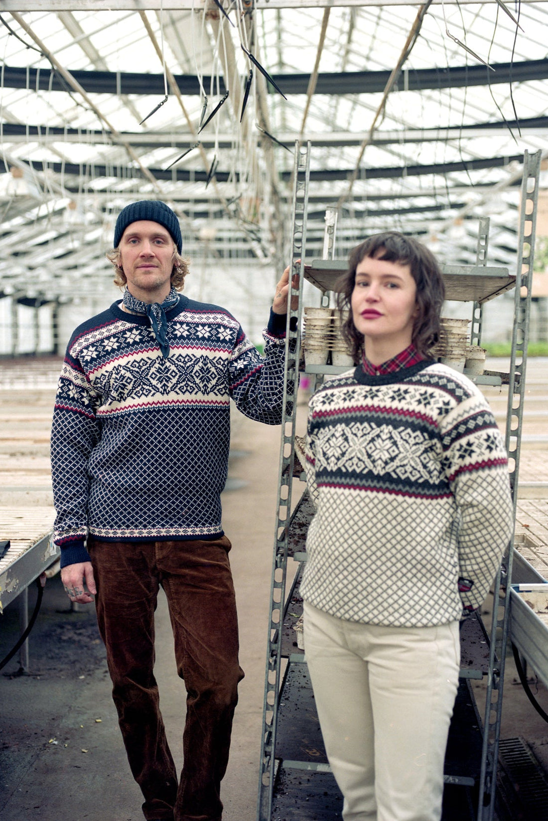 Two people wearing patterned sweaters in a greenhouse setting