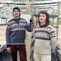 Two people wearing patterned sweaters in a greenhouse setting