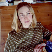 Woman wearing a patterned sweater indoors with wooden walls and books in the background