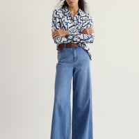 Woman wearing a patterned shirt and blue jeans on a plain background