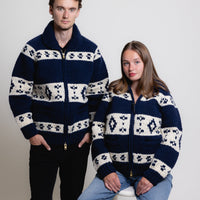 Two people wearing matching navy blue sweaters with white patterns on a plain background