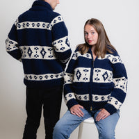 Two people wearing matching navy blue sweaters with white patterns on a white background