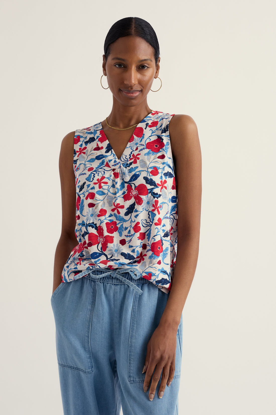 Woman wearing a floral sleeveless top and blue pants on a plain background