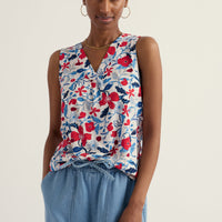 Woman wearing a floral sleeveless top and blue pants on a plain background