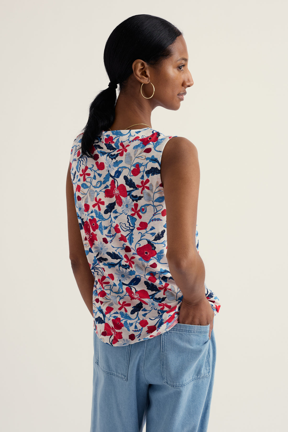 Woman wearing a sleeveless floral top and light blue pants on a plain background