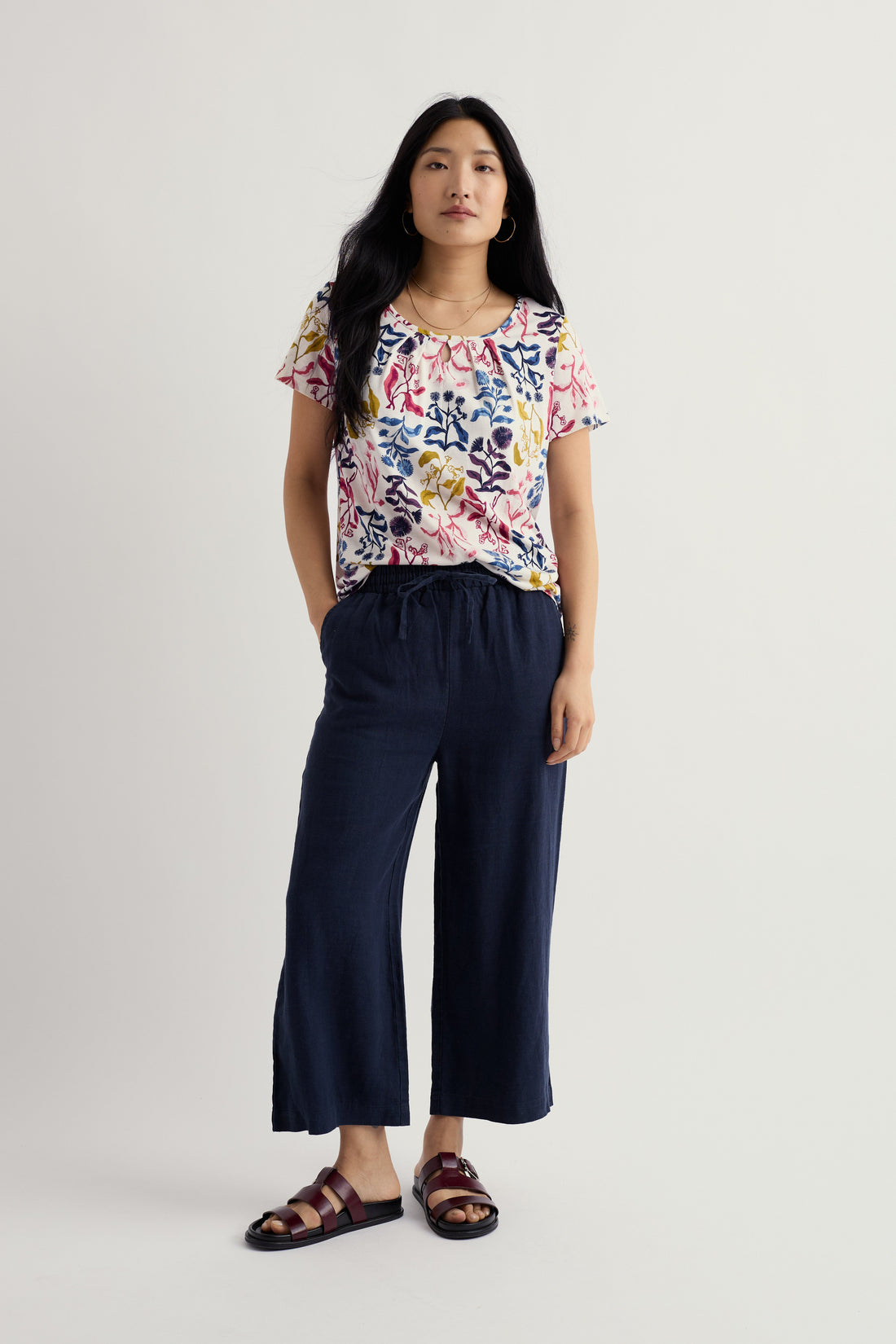 Woman wearing a colorful floral top and navy pants on a white background