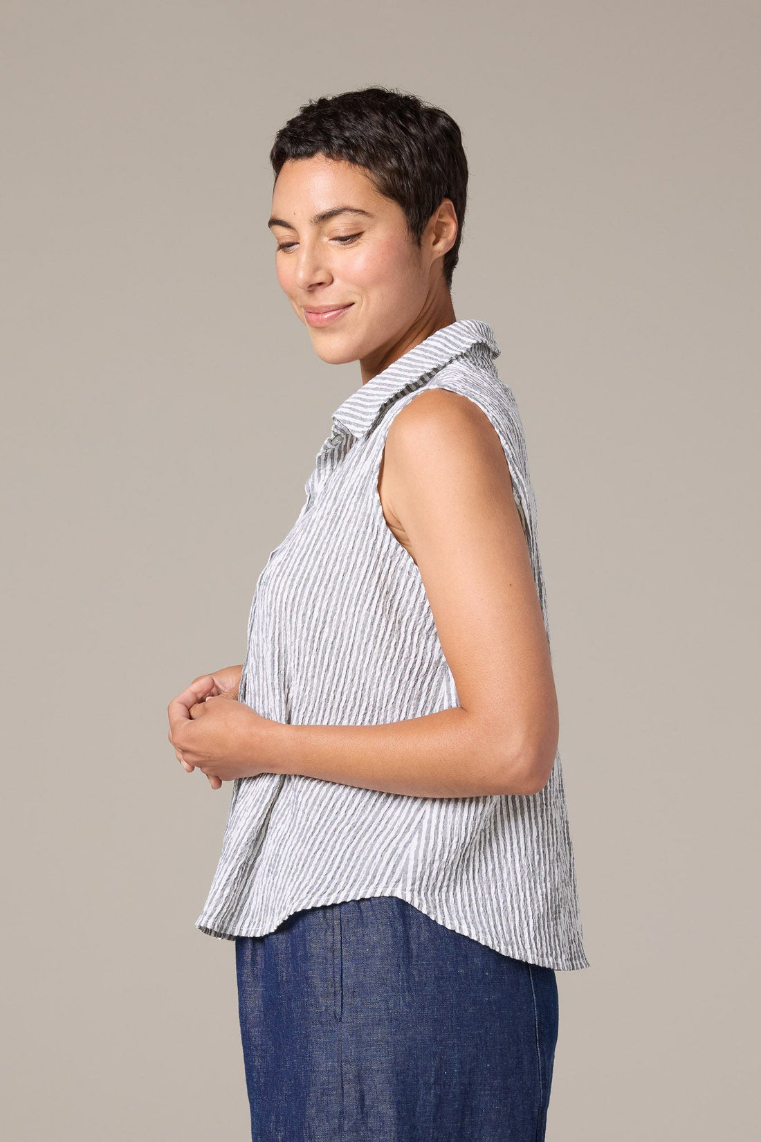 Woman wearing a sleeveless striped shirt and blue pants against a plain background