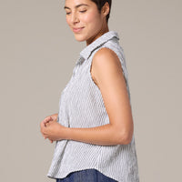 Woman wearing a sleeveless striped shirt and blue pants against a plain background
