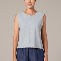 Woman wearing a light blue sleeveless top and dark blue pants against a beige background