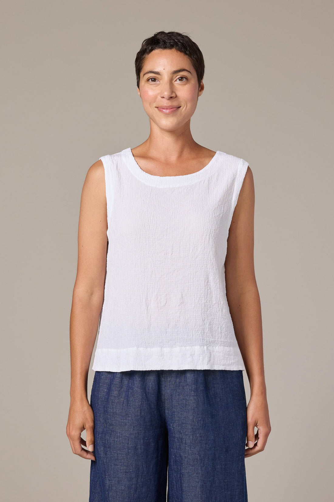Woman wearing a white sleeveless top and blue pants against a beige background