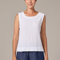 Woman wearing a white sleeveless top and blue pants against a beige background