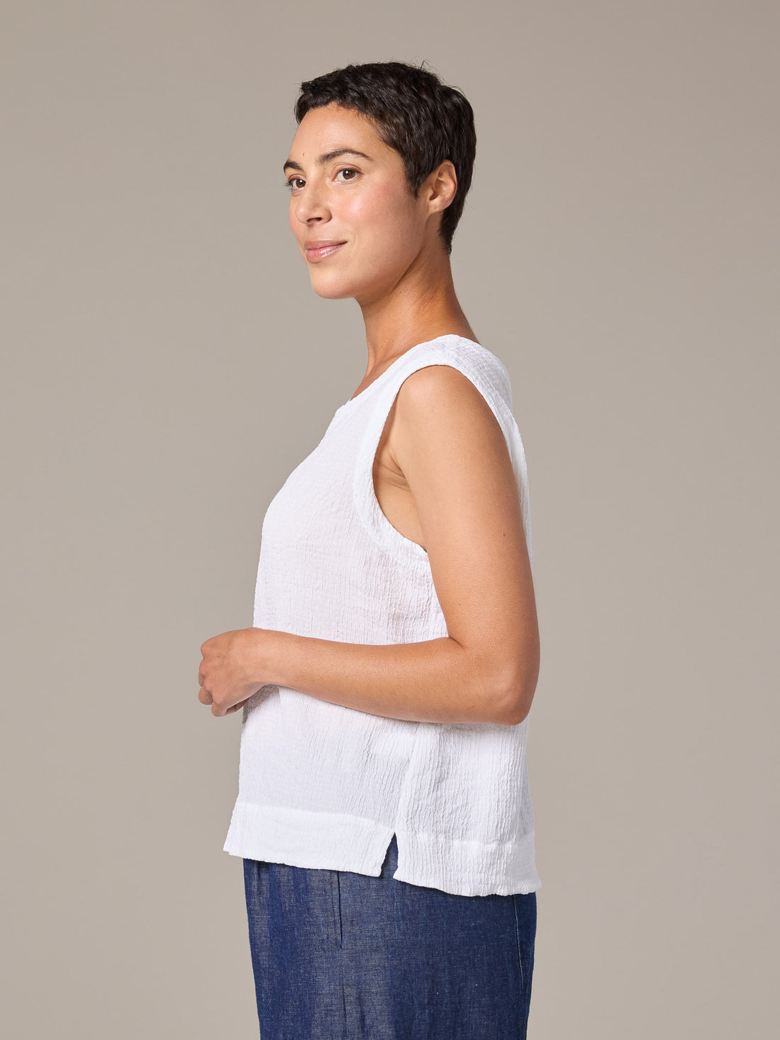 Woman wearing a white sleeveless top and blue pants against a beige background