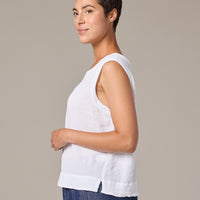 Woman wearing a white sleeveless top and blue pants against a beige background