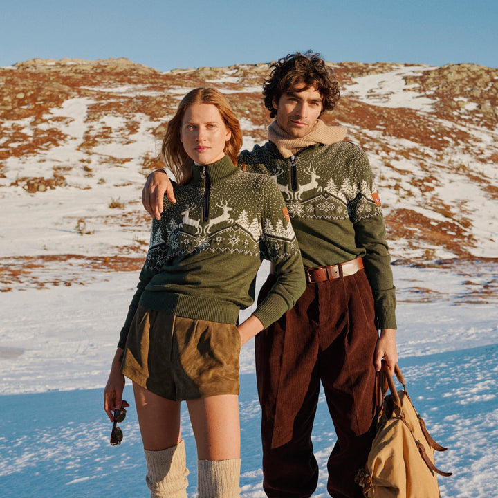 Two people in matching green sweaters standing in a snowy landscape.
