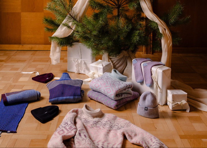 Small decorated Christmas tree with ribbons on a wooden floor, surrounded by wrapped gifts and wool knit dale of norway sweaters.