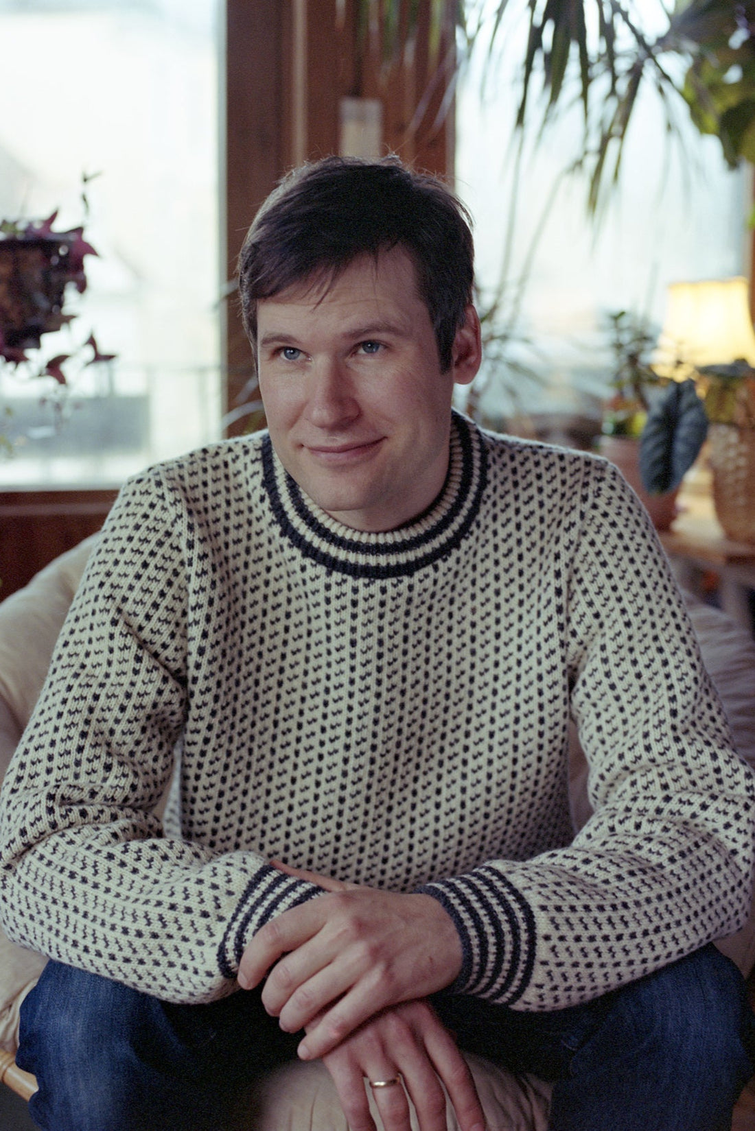 Man wearing a patterned sweater sitting indoors with a blurred background