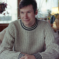 Man wearing a patterned sweater sitting indoors with a blurred background