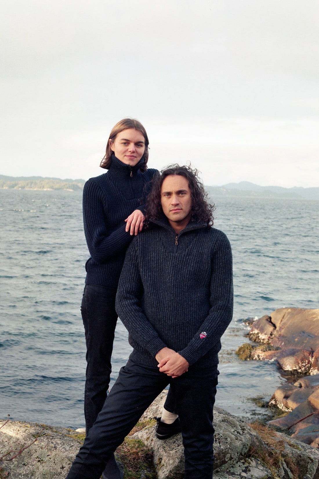 Two people standing on rocks by a body of water.