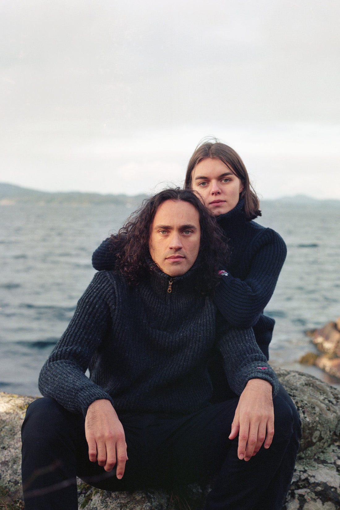 Two people sitting on rocks by a body of water.