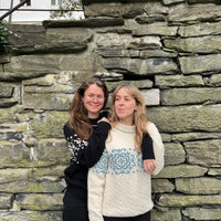 Two women standing against a stone wall with a house in the background