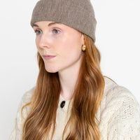 A person wearing a beige beanie hat and a cable knit sweater.