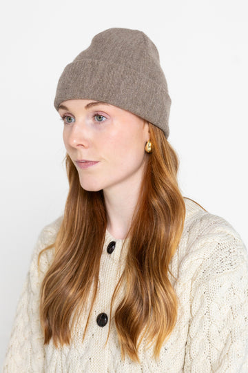 A person wearing a beige beanie hat and a cable knit sweater.