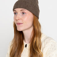 A person wearing a dark cocoa colored beanie hat.