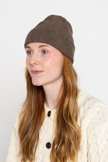 A person wearing a dark cocoa colored beanie hat.