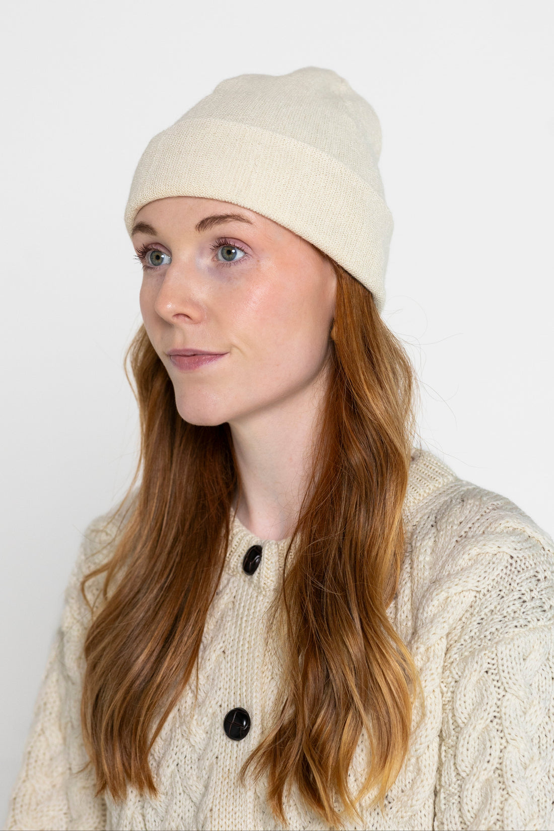 A person wearing a beige beanie hat and a knit sweater.