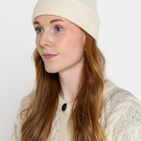 A person wearing a beige beanie hat and a knit sweater.