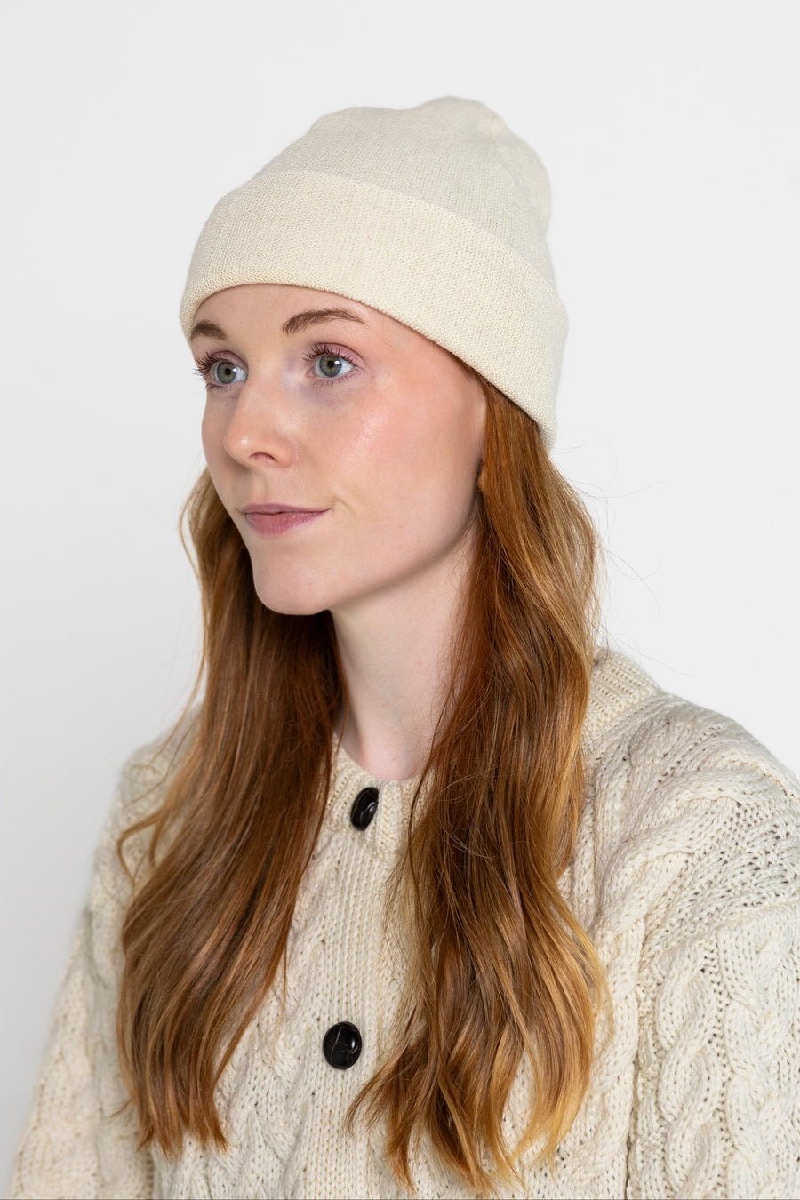 A person wearing a beige beanie hat and a knit sweater.