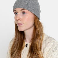 A person wearing a gray beanie hat and a white knitted cardigan against a neutral background.
