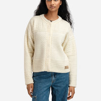 Woman wearing a cream sweater and blue jeans on a white background