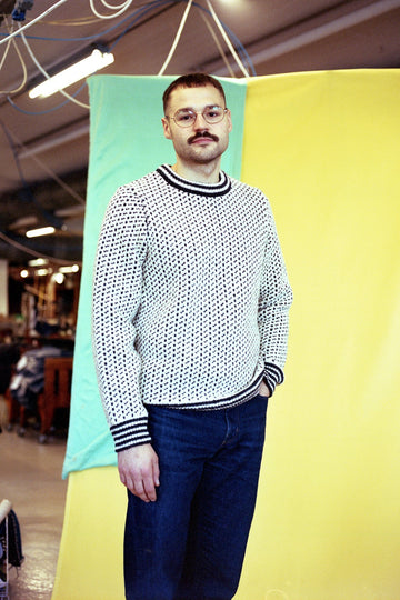 Person wearing a patterned sweater and glasses standing against a colorful background