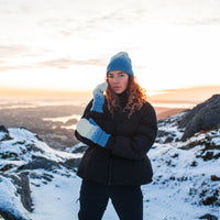 Model wears the Norlender Adult Mittens in Blue in a snowy landscape.