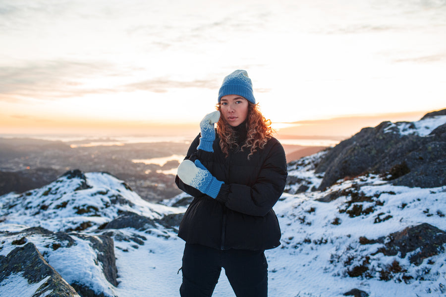 Model wears the Norlender Adult Mittens in Blue in a snowy landscape.