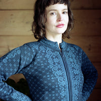 Woman wearing a blue patterned jacket indoors against a wooden wall.