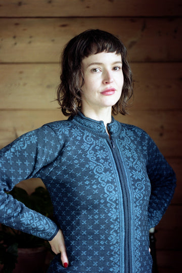 Woman wearing a blue patterned jacket indoors against a wooden wall.