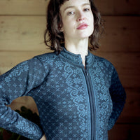 Woman wearing a blue patterned jacket against a wooden wall.