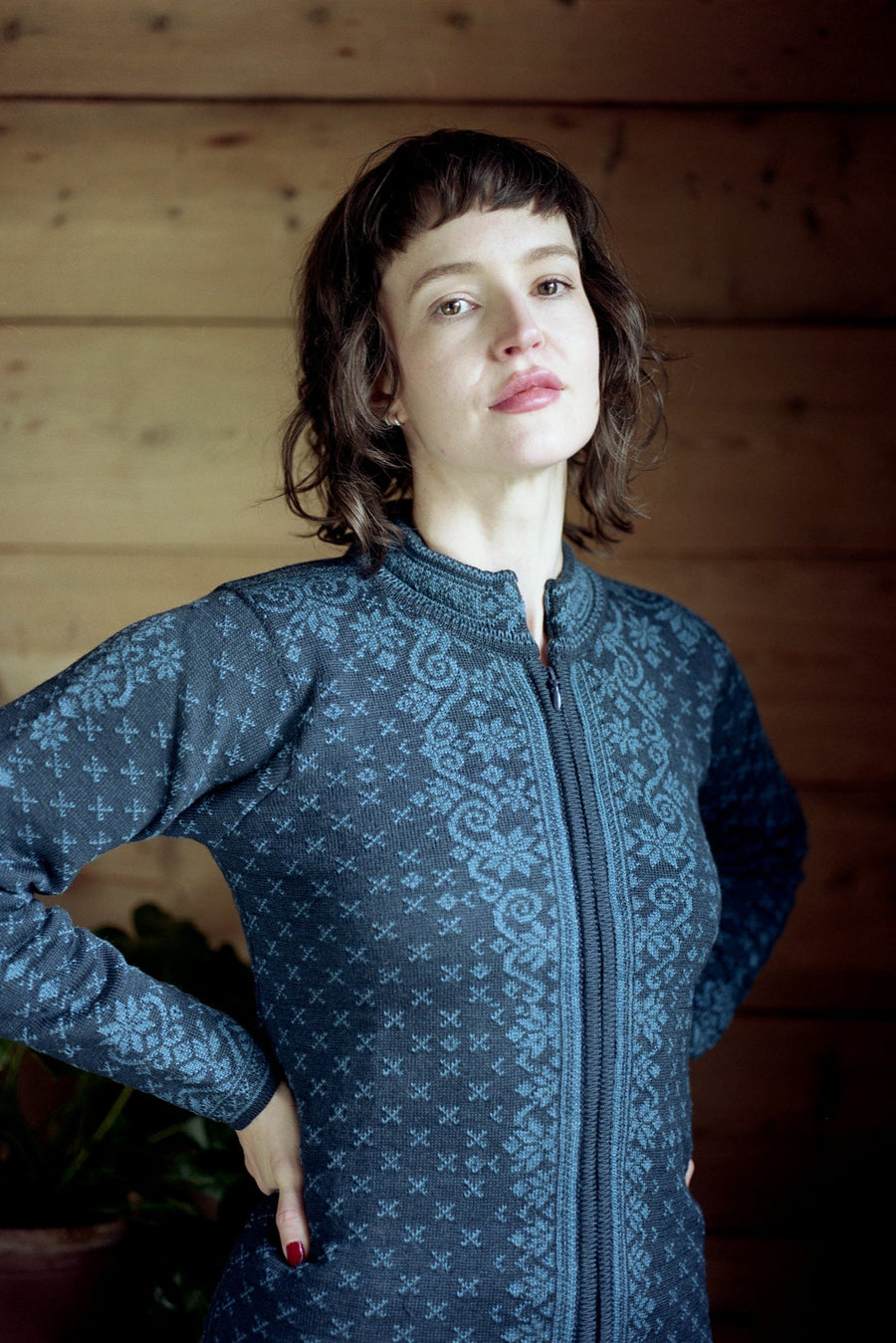 Woman wearing a blue patterned jacket against a wooden wall.