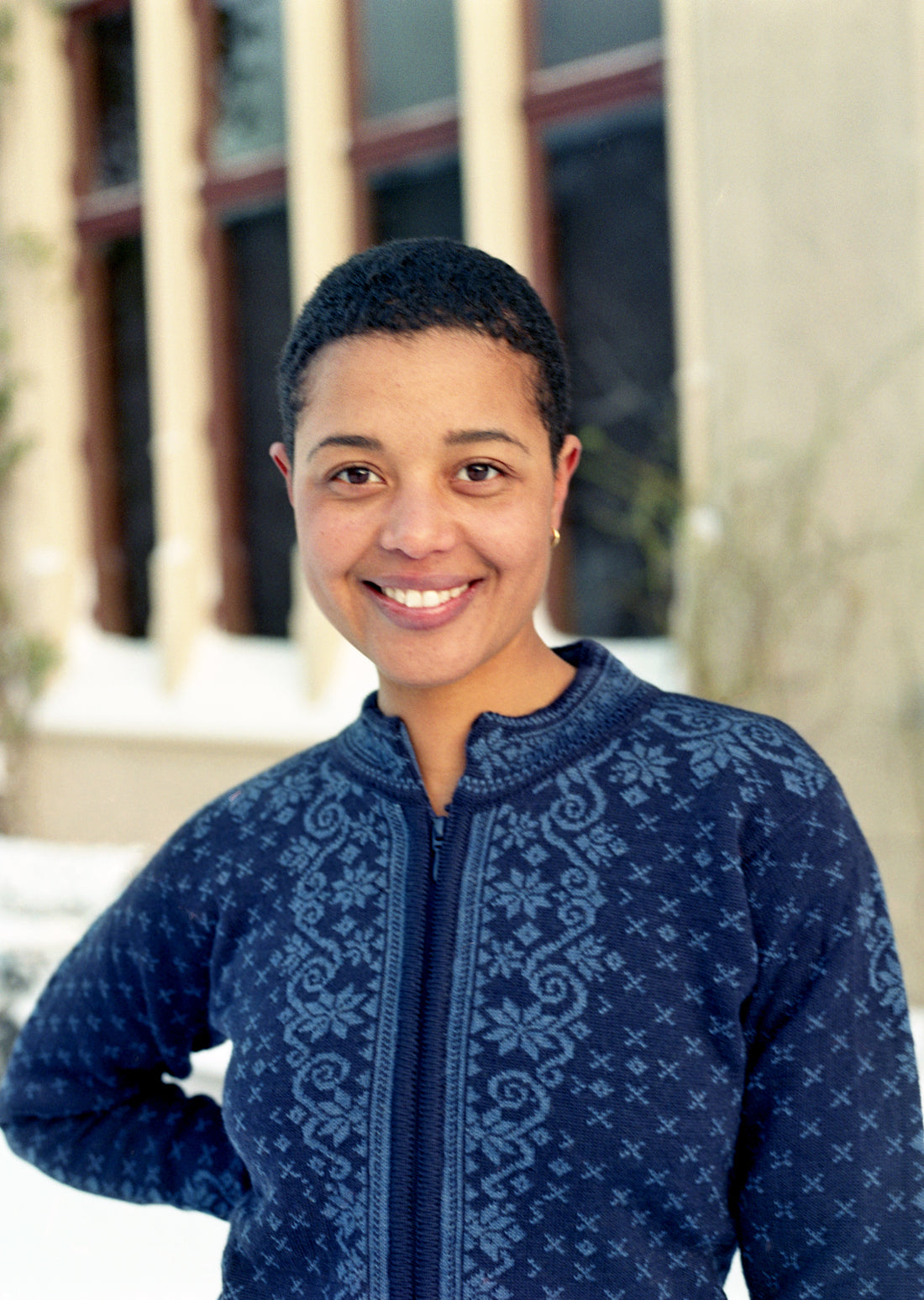 Person wearing a blue patterned sweater standing outdoors with a building in the background