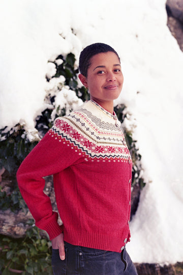 Person wearing a red sweater with a patterned yoke standing outdoors with snow and trees in the background
